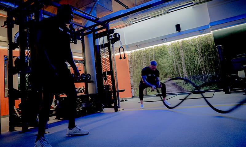 Person doing battle rope exercise in a gym with weightlifting equipment in the background.