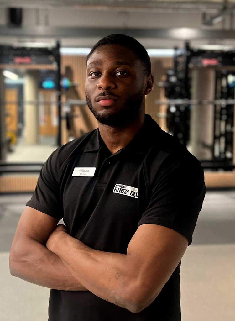 MFC trainer in black polo shirt with MFC club logo, standing in front of gym equipment.