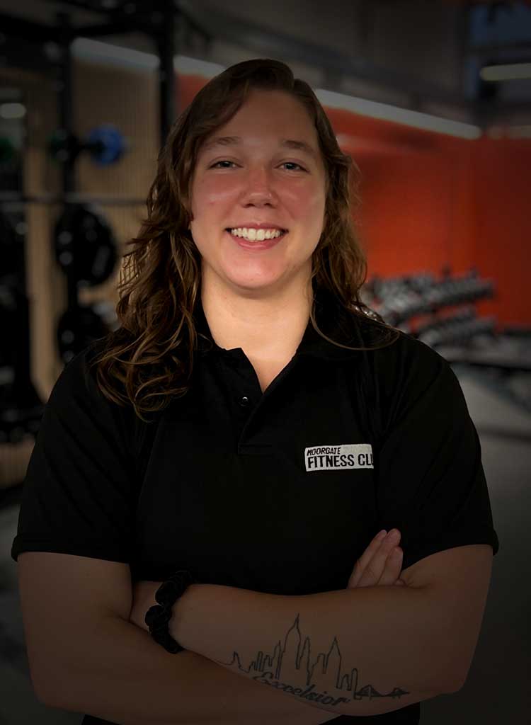 MFC trainer in black polo shirt with MFC club logo, standing in front of gym equipment.