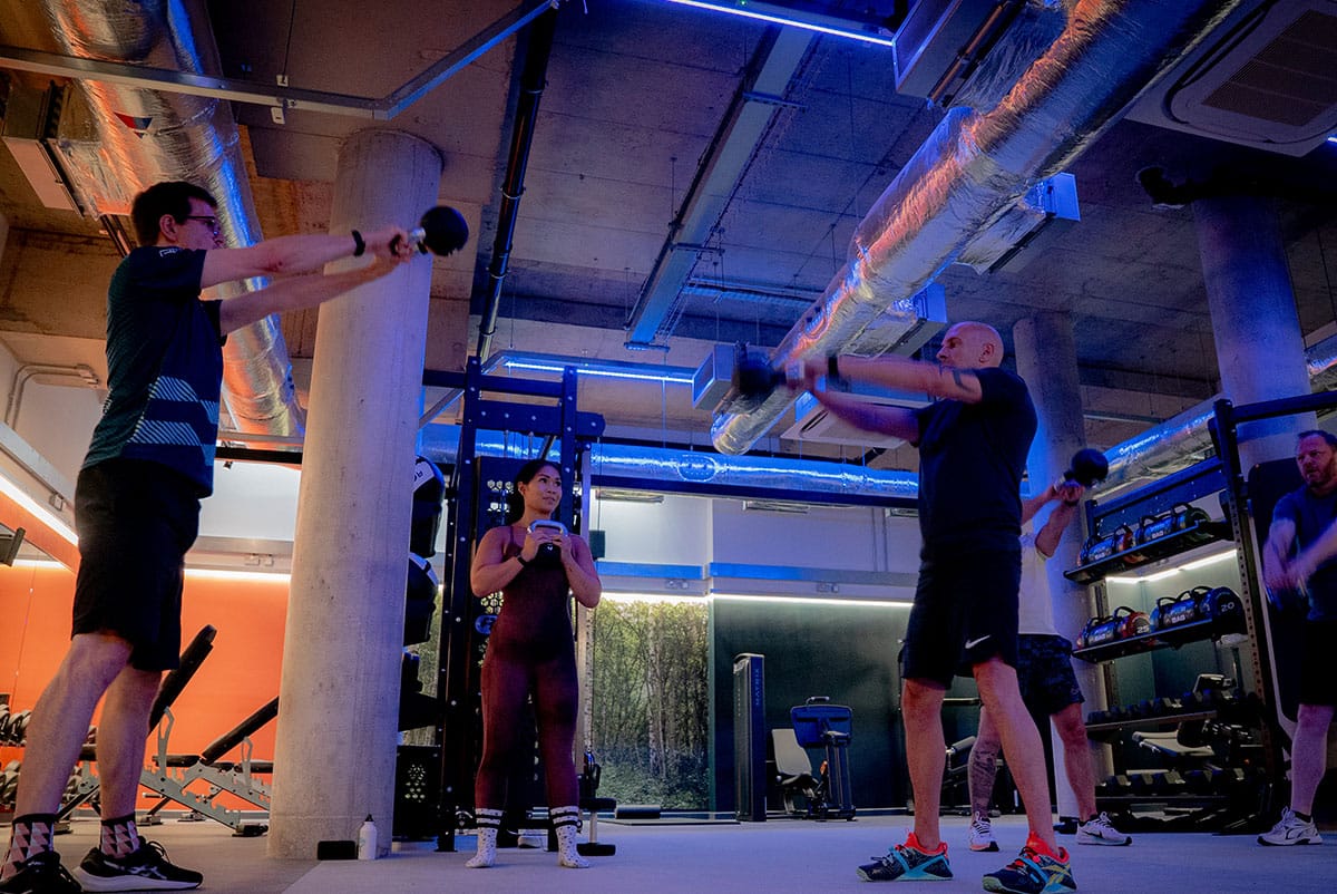 People exercising in a gym with weights and pull-up bars, illuminated by blue and orange lights.