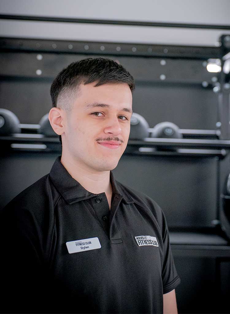 MFC trainer in black polo shirt with MFC club logo, standing in front of gym equipment.