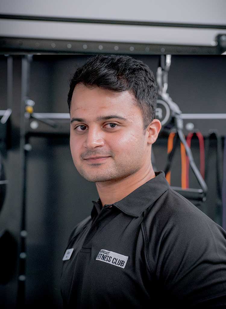 MFC trainer in black polo shirt with MFC club logo, standing in front of gym equipment.