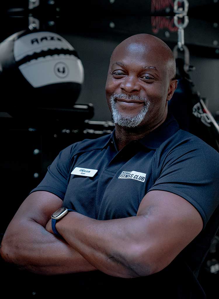 MFC trainer in black polo shirt with MFC club logo, standing in front of gym equipment.